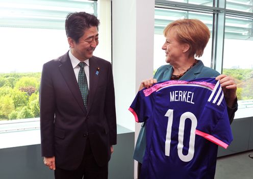 Photograph of Prime Minister Abe presenting a Japanese national team uniform to H.E. Dr. Angela Merkel, Federal Chancellor of the Federal Republic of Germany