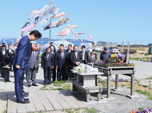 Photograph of the Prime Minister offering a silent bow in front of the “Ganbaro! Ishinomaki” signboard