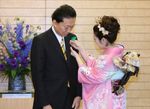 Photograph of the Prime Minister having a green feather pin attached by the Japan Cherry Blossom Queen