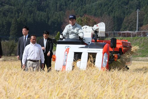 Photograph of the Prime Minister harvesting rice using a combine at a production area for premium brand rice