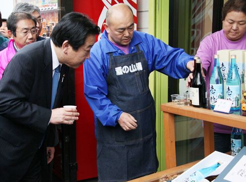 Photograph of the Prime Minister sampling locally-brewed sake in the shopping district in Suehiro-cho
