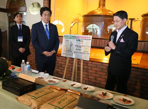 Photograph of the Prime Minister receiving an explanation regarding local specialties offered as gifts to hometown taxpayers as a means to promote regional industry