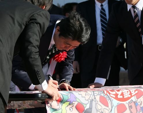 Photograph of the Prime Minister signing his name on the reconstruction flag at the opening ceremony for JR Shinchi Station