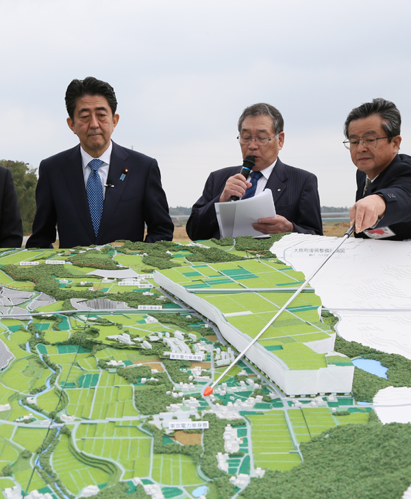 Photograph of the Prime Minister observing a map of the Ogawara Reconstruction Hub area
