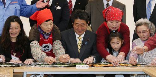 Photograph of the Prime Minister making jumbo seaweed rolls with other participants at an assembly hall