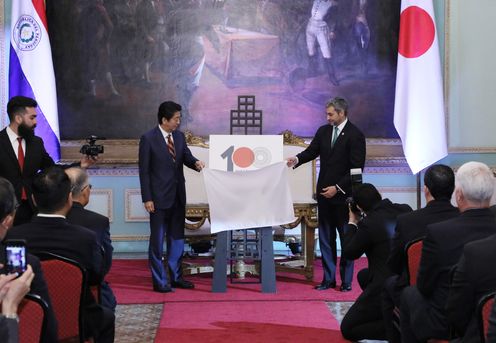Photograph of the two leaders unveiling the logo commemorating 100 years of diplomatic relations between Japan and Paraguay