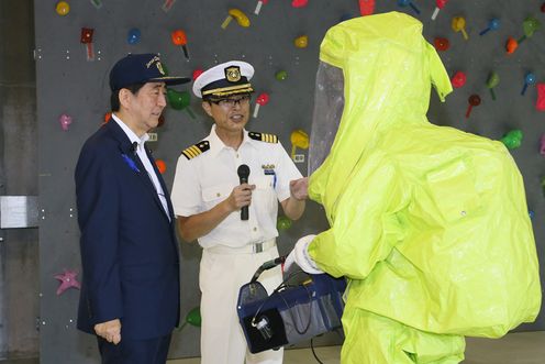 Photograph of the Prime Minister listening to an explanation of the contamination containment drill from a member of the Japan Coast Guard