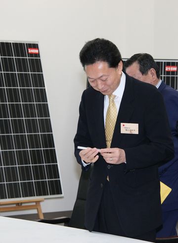 Photograph of the Prime Minister listening to an explanation with a solar panel in the background