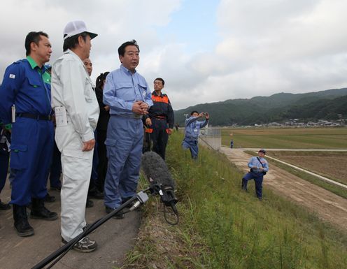 Photograph of the Prime Minister observing the flood damage in Ozato, Kiho Town, atop a levee